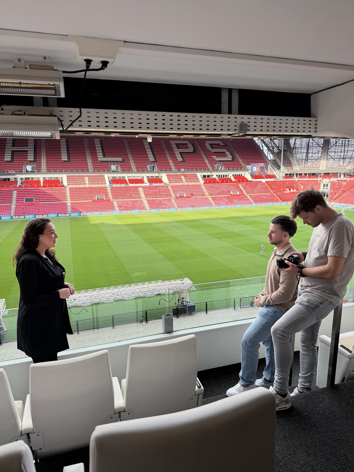 Lisette Lucas met interviewer en videograaf tijdens een testimonialopname in een skybox van het Philips Stadion